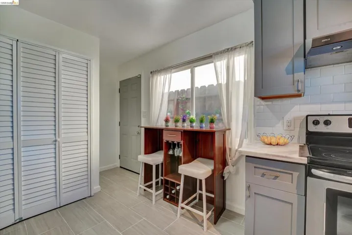 Light gray tile flooring, crisp white subway tile backsplash, light gray cabinetry, and a stainless steel oven with a range hood