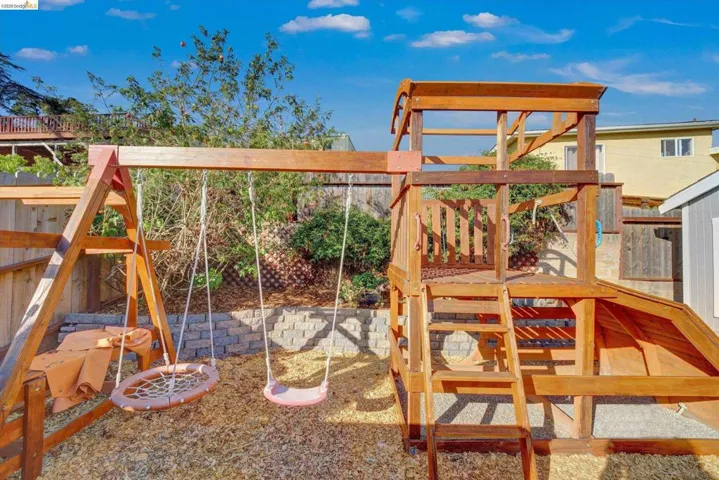Outdoor play structure with a slide, swings, and an elevated platform, set on a wood chip surface
