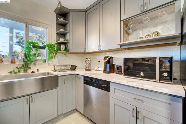 Stainless steel apron-front sink, light gray cabinetry, white subway tile backsplash, light-toned countertop, and stainless steel dishwasher