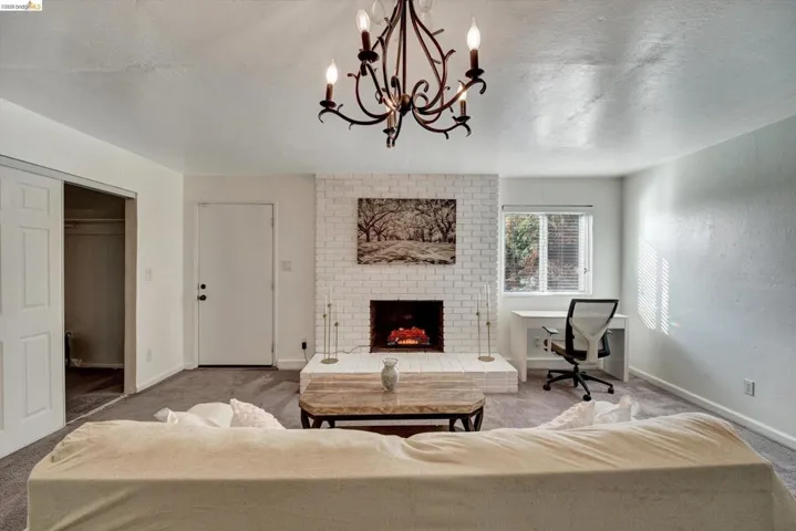 Living space featuring a whitewashed brick fireplace, gray carpeting, a built-in window desk, and a decorative chandelier