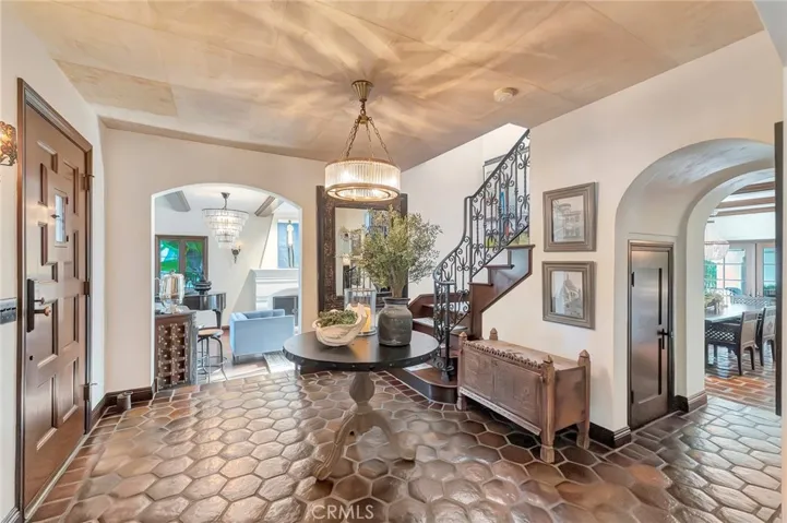 A grand Living room with high ceilings steps down from the Foyer, with views of all the lush landscaped grounds front and rear, with French Doors walking directly to the private oasis with green grass raised gardens pool spa firepit fireplace, and loggia with heated dining and sitting areas under cover with large arches to enjoy a pool view