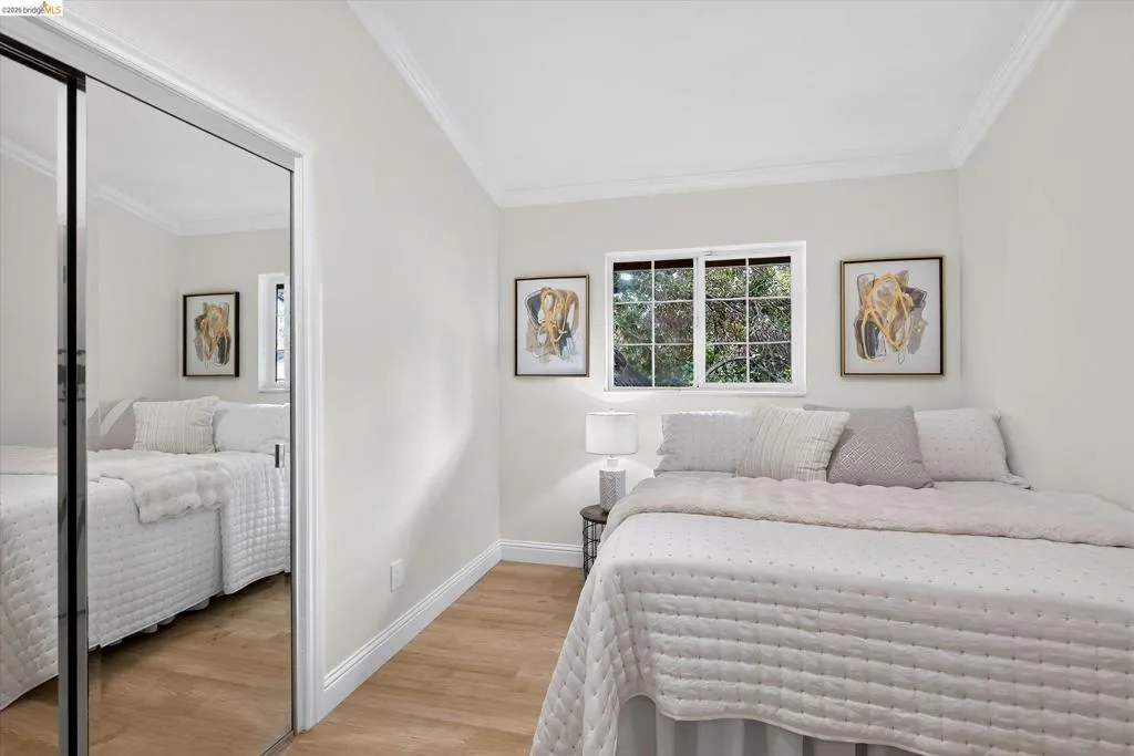 Wood-finish flooring, white crown molding, mirrored closet doors, and white paneled walls