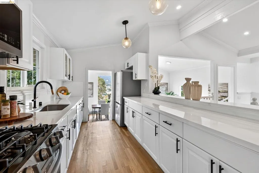 White shaker cabinetry with dark hardware, stainless steel appliances, light-toned countertops, wood-finish flooring, and a gas range