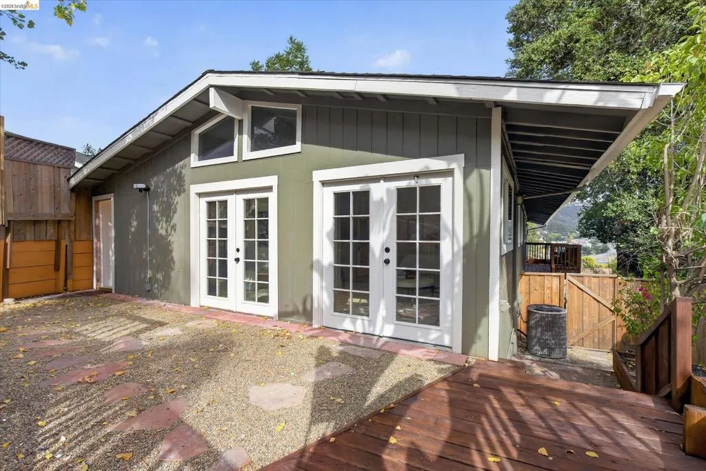 Exterior featuring multiple sets of glass French doors, transom windows, a wood-finish deck, and a gravel-covered patio