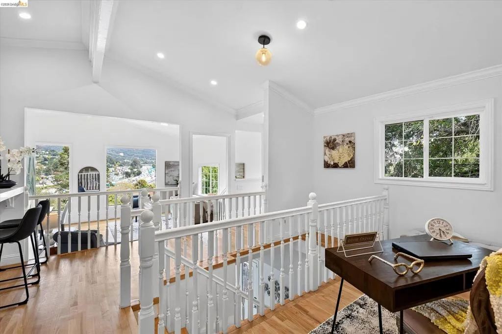 Hardwood flooring throughout, white baluster railing, vaulted ceilings, recessed lighting, and multiple windows