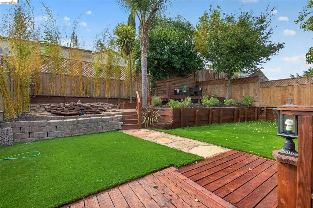 Expansive backyard featuring a wood deck, artificial turf, stone paver pathway, retaining walls, and tiered landscaping