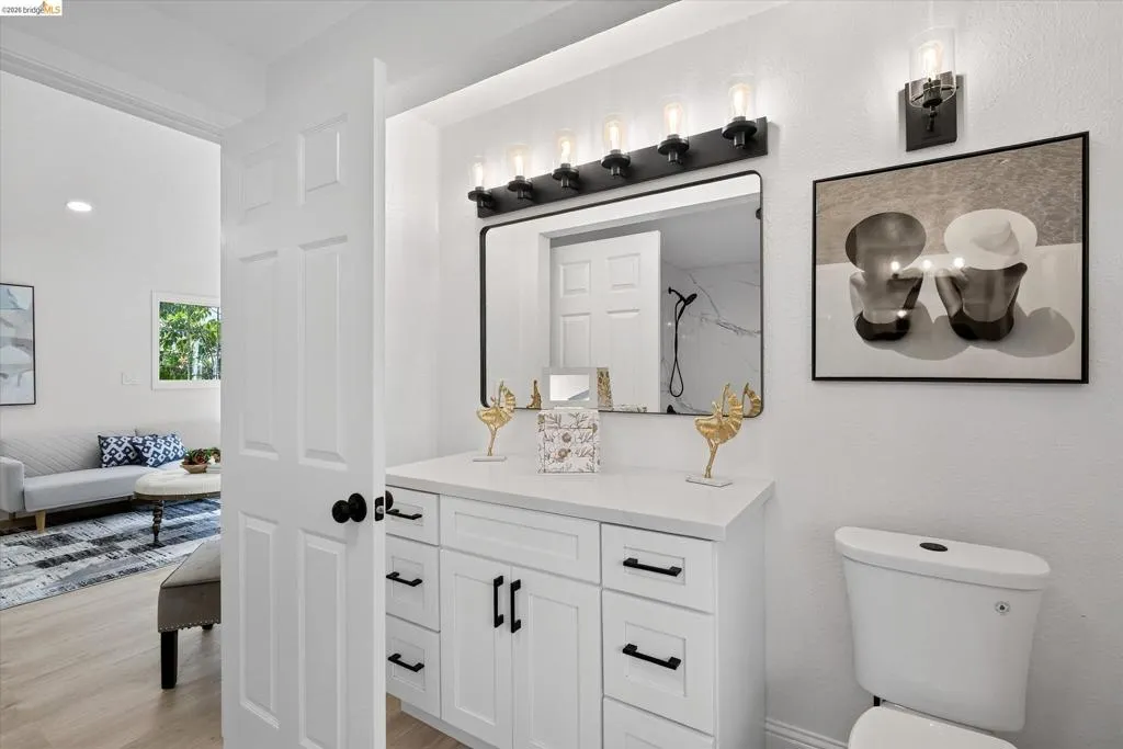 White shaker vanity with black hardware, complementing black-framed mirror, and a multi-bulb vanity light fixture