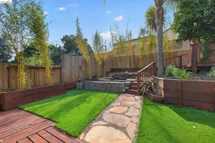 Tiered backyard with wood-finish decking, artificial turf, and a flagstone pathway