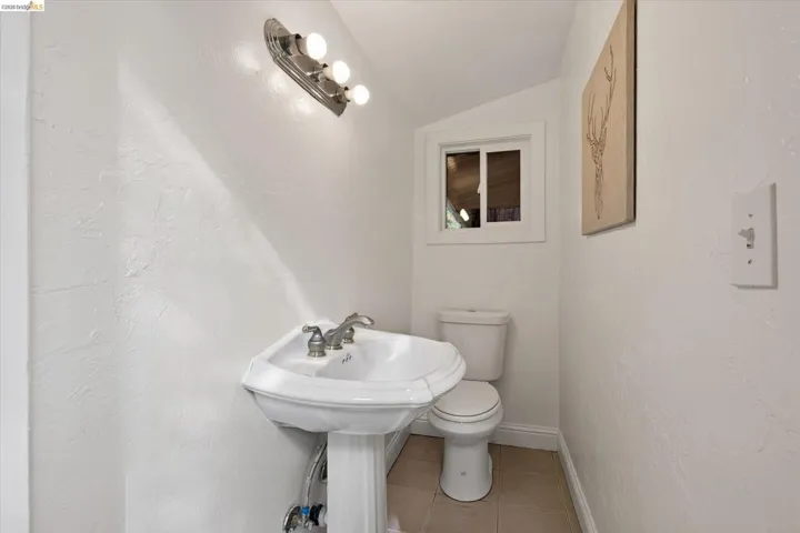 Pedestal sink with dual-handle faucet, wall-mounted vanity lighting, and a white toilet