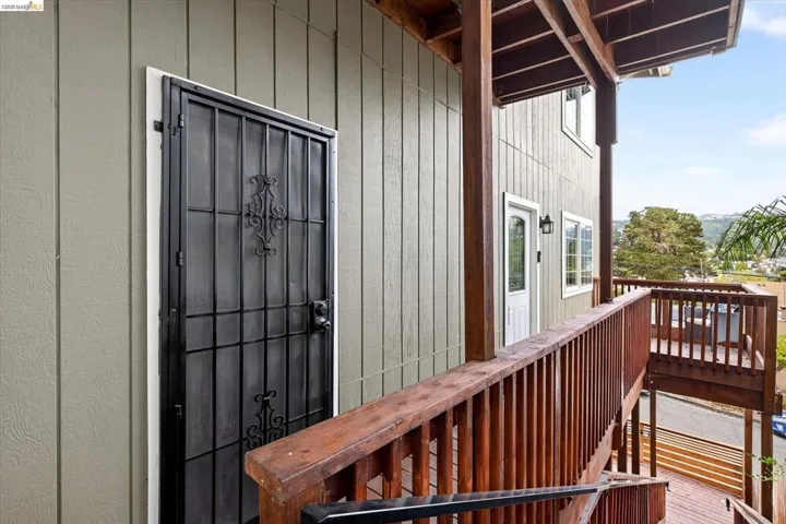 Board and batten siding, dark wood-finish railings, exterior security door, additional exterior door, and double-pane windows