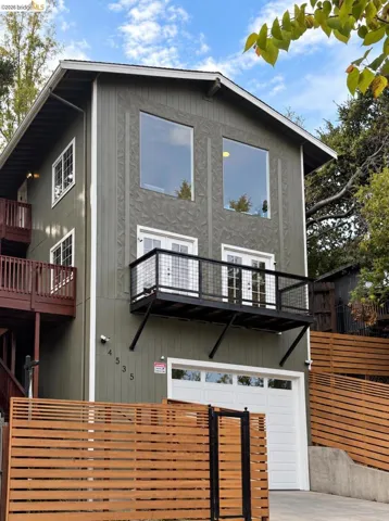 Multi-level exterior with a private balcony, wood slatted fencing, an attached garage, and upper-level picture windows