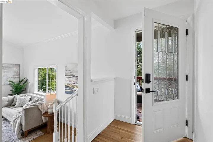 Frosted glass entry door with matte black hardware, wood-finish flooring, white painted walls, and white baluster railing
