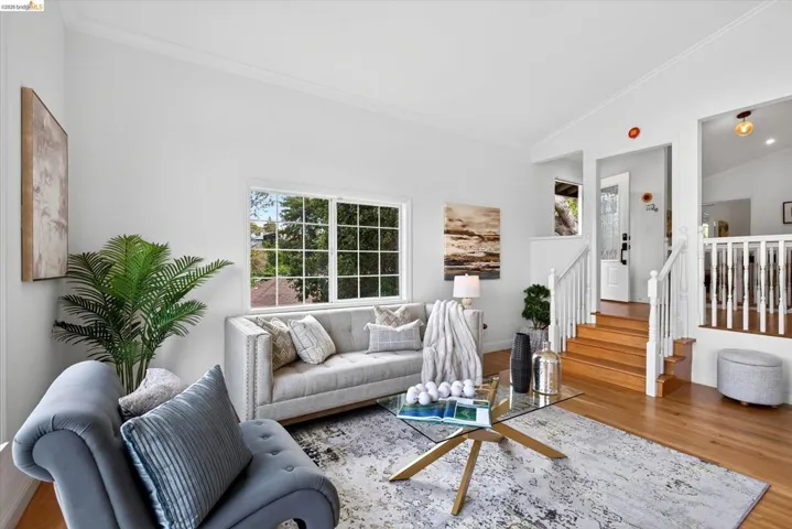 Hardwood flooring, white crown molding, large window with grid pattern, white baluster staircase, and a glass paneled door