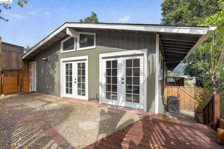 Exterior featuring multiple sets of glass French doors, transom windows, a wood-finish deck, and a gravel-covered patio