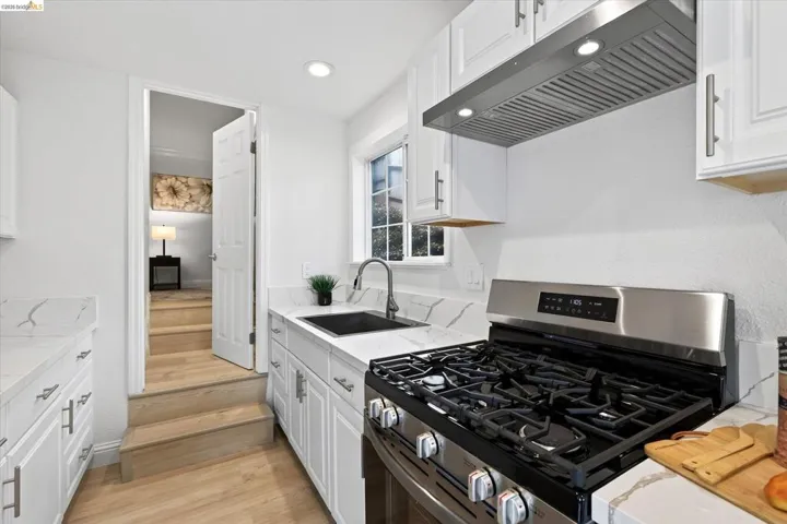 White shaker cabinetry complemented by brushed nickel hardware, a stainless steel gas range with coordinating hood, a black undermount sink, and light-toned wood-finish flooring