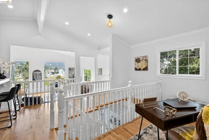 Hardwood flooring throughout, white baluster railing, vaulted ceilings, recessed lighting, and multiple windows