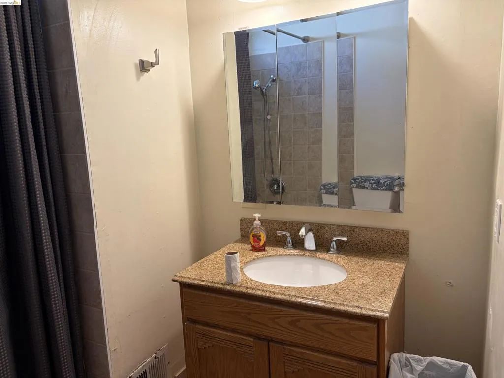 Vanity with an integrated sink, granite-style countertop, wood-finish cabinetry, and an overhead mirrored medicine cabinet