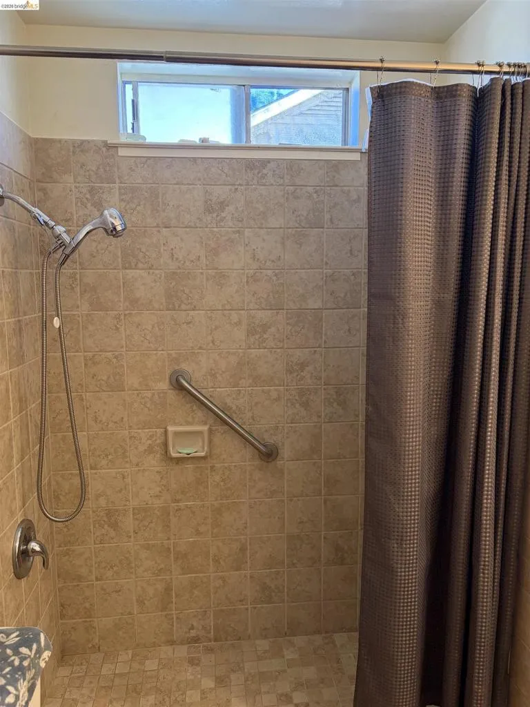 Tiled shower surround with a handheld shower head, grab bar, and high-set window