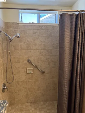 Tiled shower surround with a handheld shower head, grab bar, and high-set window