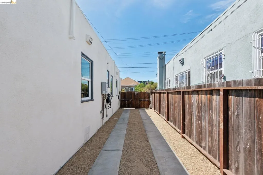 Gravel driveway with concrete tire tracks, wooden privacy fence, and rear gate access Gravel driveway with concrete tire tracks, wooden privacy fence, and rear gate access