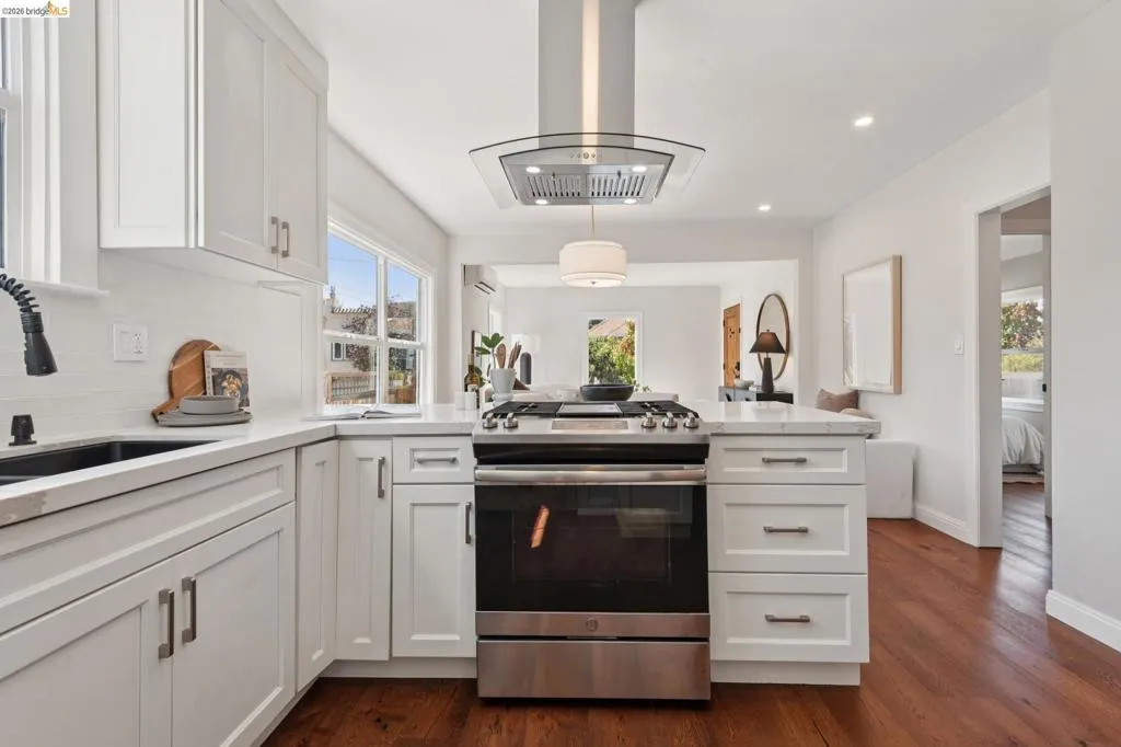 White shaker cabinetry, stainless steel range with overhead hood, wood-finish flooring, white countertops, and a subway tile backsplash White shaker cabinetry, stainless steel range with overhead hood, wood-finish flooring, white countertops, and a subway tile backsplash