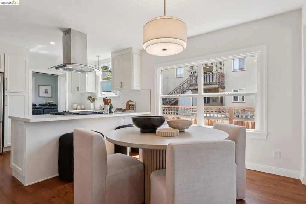 Open-concept kitchen with white cabinetry, stainless steel range hood, stone countertops, and wood-finish flooring Open-concept kitchen with white cabinetry, stainless steel range hood, stone countertops, and wood-finish flooring