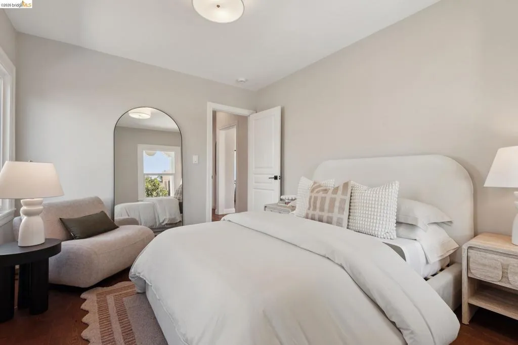 Wood-finish flooring, white paneled door with black hardware, arched full-length mirror, and overhead flush-mount lighting Wood-finish flooring, white paneled door with black hardware, arched full-length mirror, and overhead flush-mount lighting