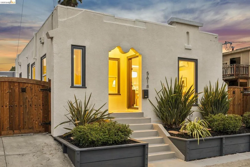 Stucco exterior with an arched entryway, dark-framed windows, and built-in planters with established landscaping Stucco exterior with an arched entryway, dark-framed windows, and built-in planters with established landscaping