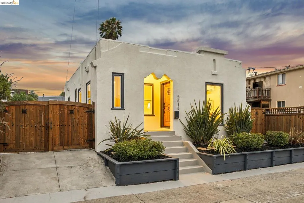 Stucco exterior with dark trim windows, arched entry, concrete steps, and dark-stained wood privacy fencing Stucco exterior with dark trim windows, arched entry, concrete steps, and dark-stained wood privacy fencing