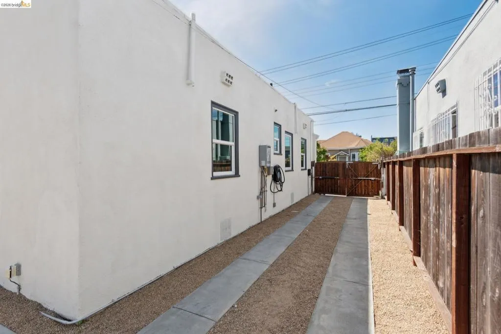 White stucco exterior, dark-framed windows, gravel and concrete pathway, wood fence, and secured gate White stucco exterior, dark-framed windows, gravel and concrete pathway, wood fence, and secured gate