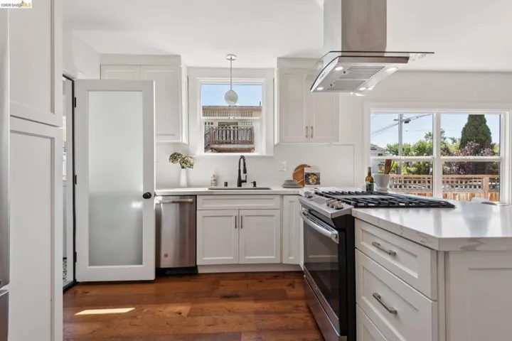 White shaker cabinetry with ample storage, stainless steel appliances, a modern range hood, expansive countertops, and wood-finish flooring