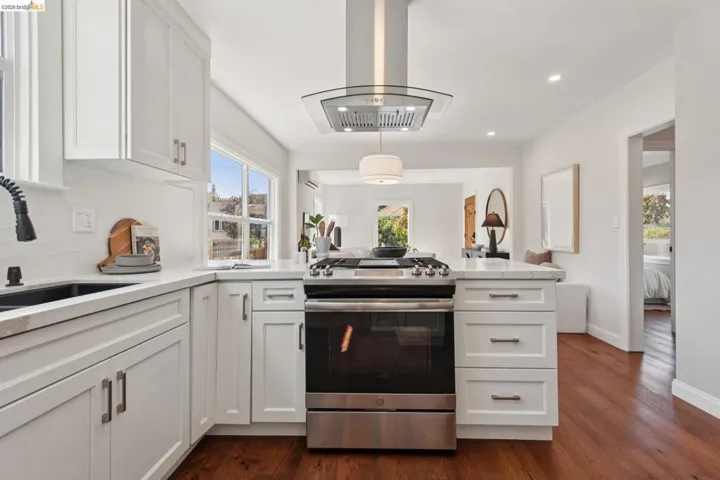White shaker cabinetry, stainless steel range with overhead hood, wood-finish flooring, white countertops, and a subway tile backsplash