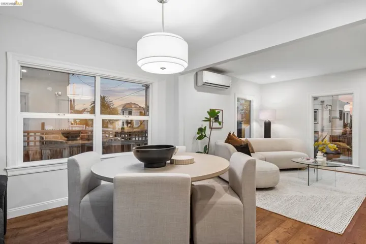 Open-concept living space with wood-finish flooring, a contemporary drum pendant light, large windows, and a wall-mounted climate control unit