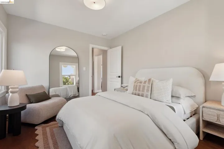 Wood-finish flooring, white paneled door with black hardware, arched full-length mirror, and overhead flush-mount lighting