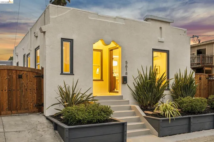 Stucco exterior with an arched entryway, dark-framed windows, and built-in planters with established landscaping