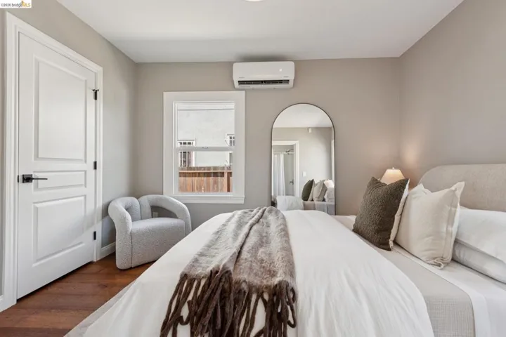 Hardwood-finish flooring, white paneled door with black hardware, window with white trim, and a wall-mounted climate control unit