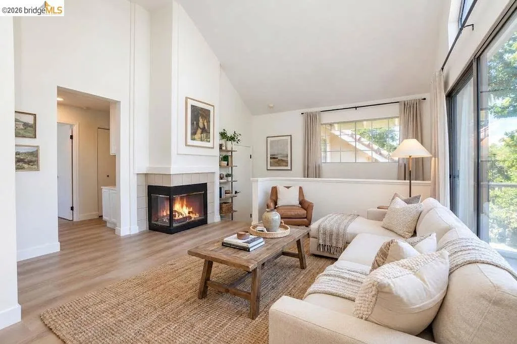 Vaulted ceiling with decorative trim, corner fireplace featuring a dark firebox and light tile surround, wood-finish flooring, and expansive glass sliding door