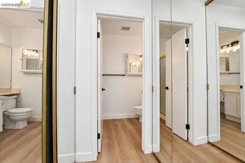 Wood-finish flooring throughout, white interior doors with black hardware, and mirrored closet doors