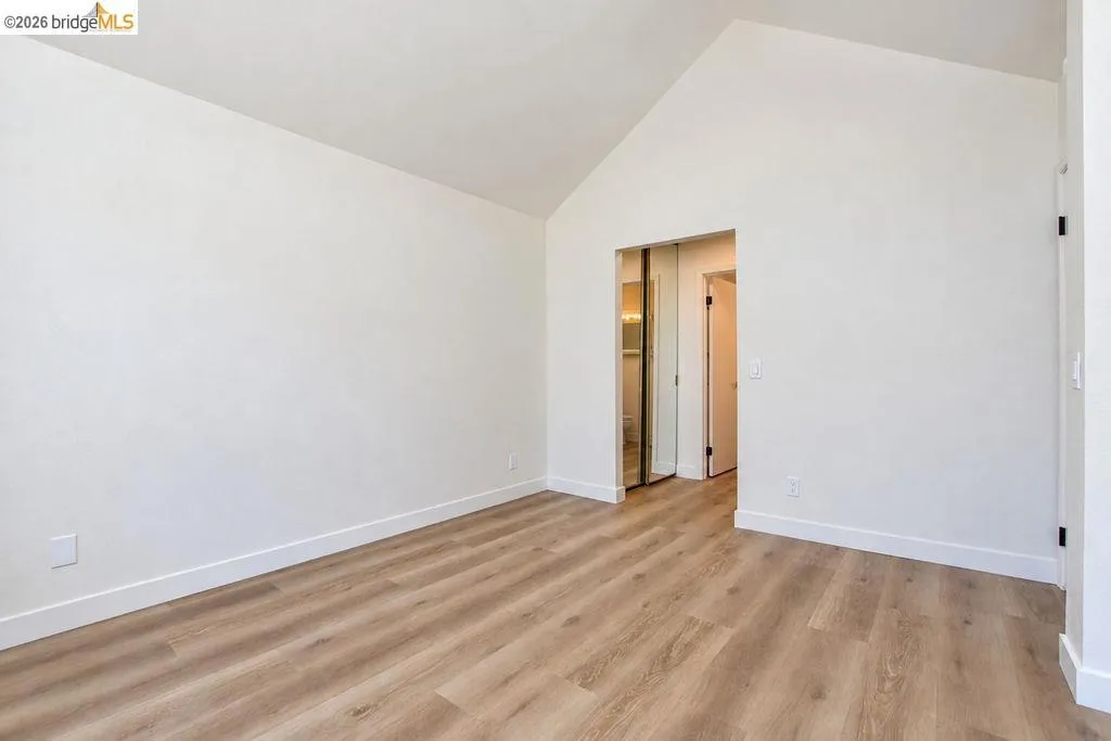 Vaulted ceiling, wood-finish flooring, white walls, and mirrored closet doors