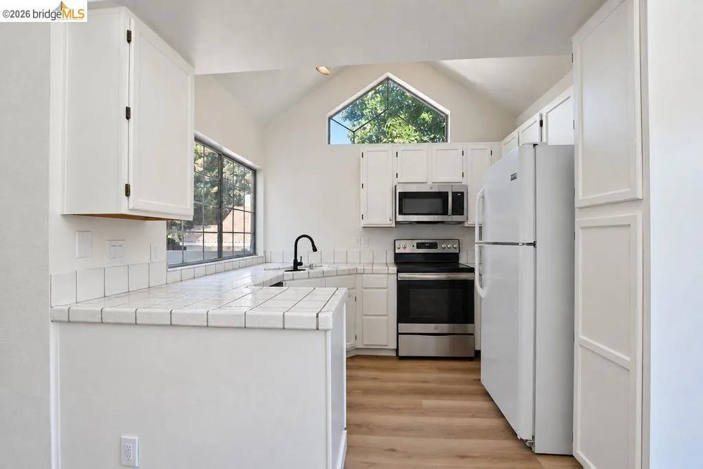 Kitchen featuring white cabinetry, tile countertops, stainless steel appliances, and wood-finish flooring