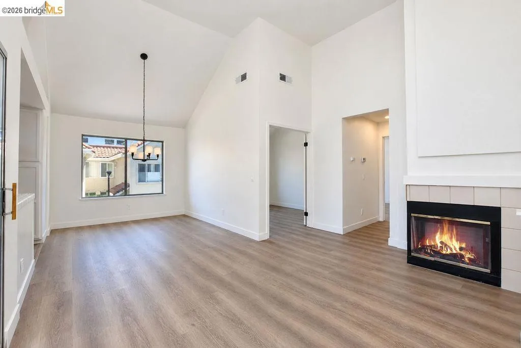 Vaulted ceilings, wood-finish flooring, a contemporary chandelier, a large window, and a tiled fireplace