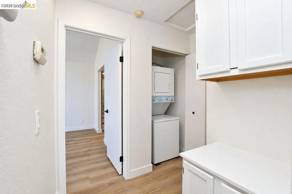 Laundry area featuring a stackable washer and dryer, white shaker-style cabinetry, and wood-finish flooring