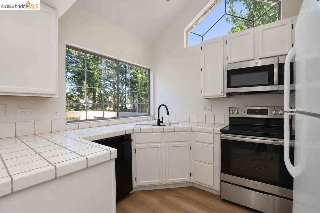 Kitchen with vaulted ceiling, wood-finish flooring, white cabinetry, and stainless steel appliances including a microwave and range