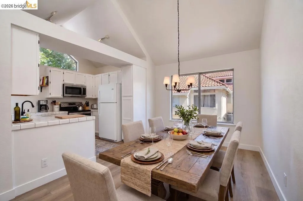 Vaulted ceilings with exposed beams, wood-finish flooring, white cabinetry, a built-in microwave, and a window with natural light
