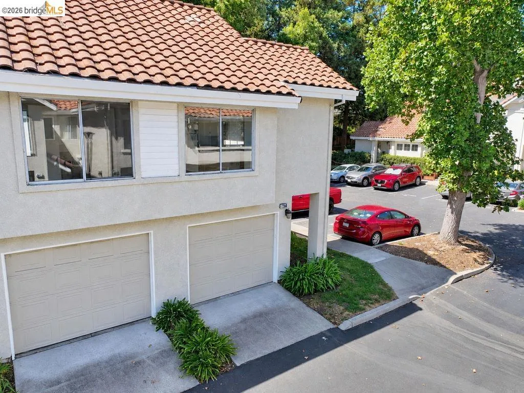 Stucco exterior with a terracotta tile roof, dual garage doors, and mature trees