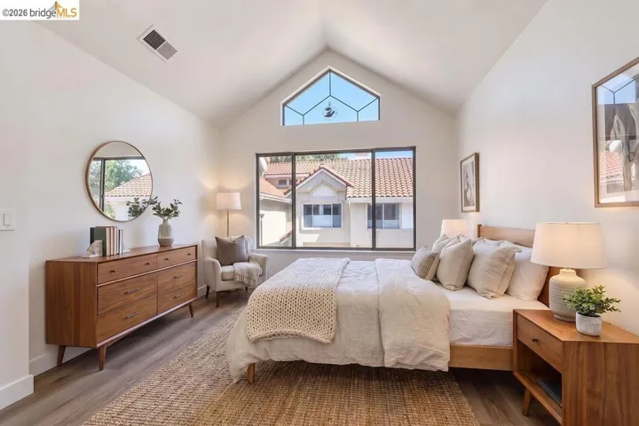 Vaulted ceiling, high transom window, large picture window, wood-finish flooring, and white walls