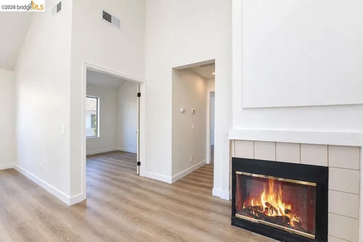 Vaulted ceiling, wood-finish flooring, white walls, and a fireplace with a tile surround