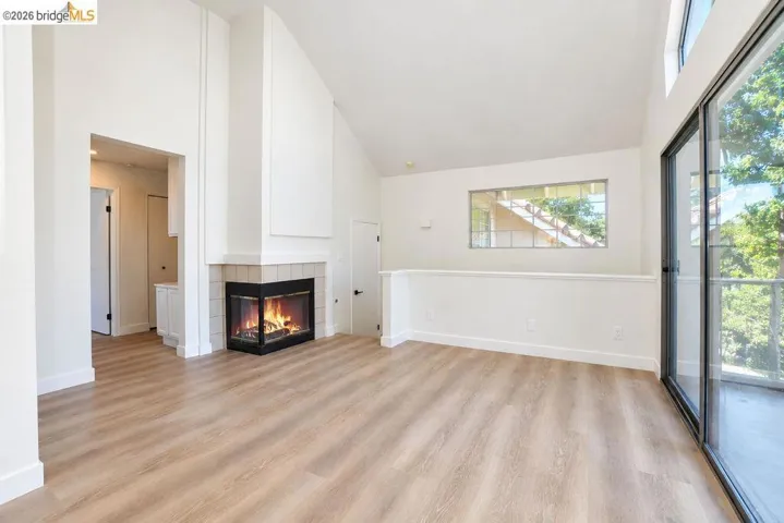 Vaulted ceiling, corner fireplace with tile surround, wood-finish flooring, sliding glass door, and clerestory window