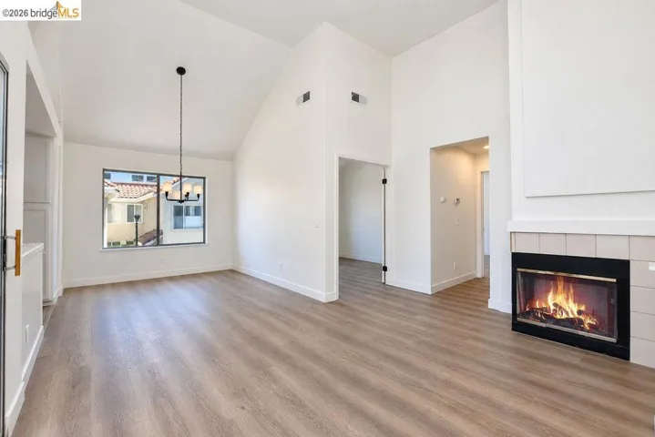 Vaulted ceilings, wood-finish flooring, a contemporary chandelier, a large window, and a tiled fireplace
