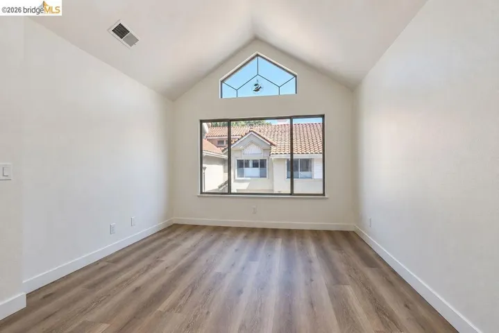 Vaulted ceiling featuring a geometric transom window, large picture window, and wood-finish flooring
